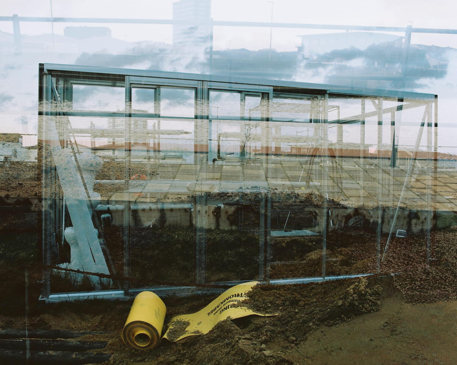 Double exposure of a greenhouse and an excavation pit in a building site.