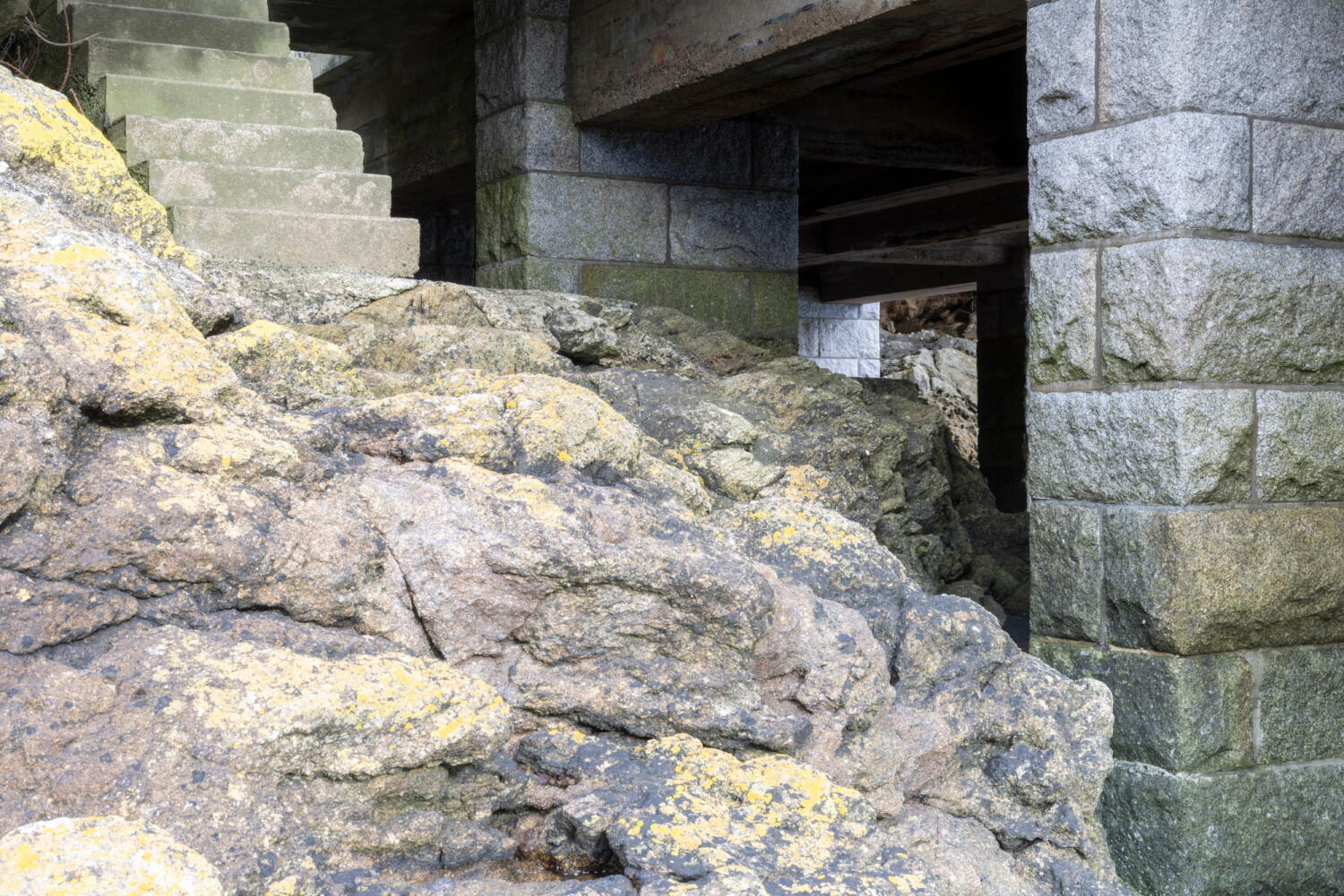 Stairs and rocks covered with green algae and rusted reinforced concrete pillars in the tidal zone.