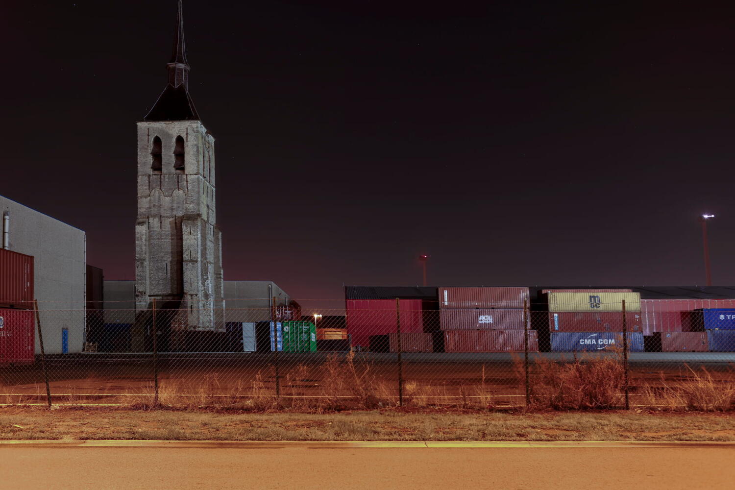 Bell tower surrounded by containers from the “Night Beasts” series. At night, these industrial installations transform into fantastical creatures that form a bestiary.