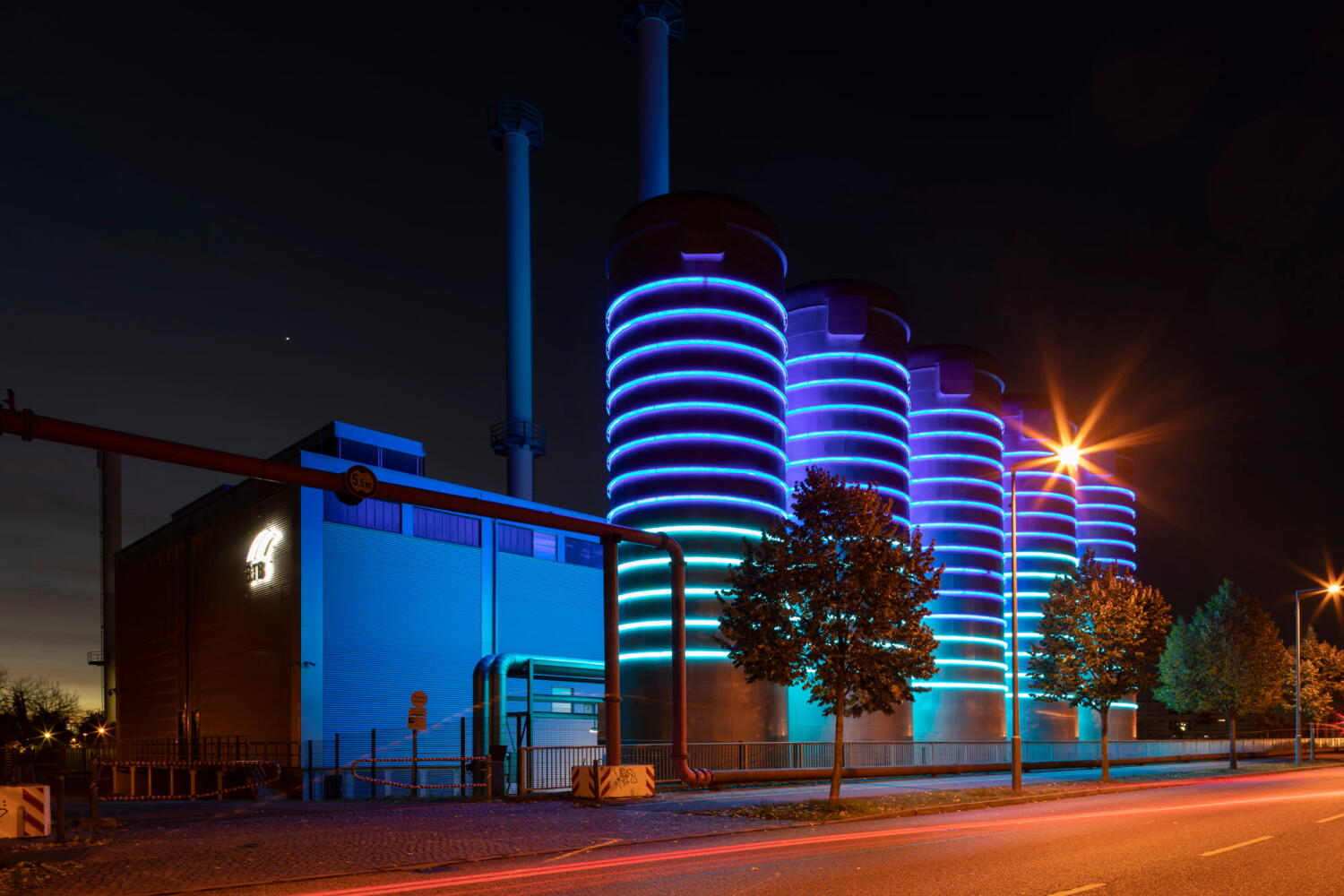 Blue illuminated silos from a factory from the series “Night Beasts.” During the night, these industrial installations transform into fantastic creatures that form a bestiary.